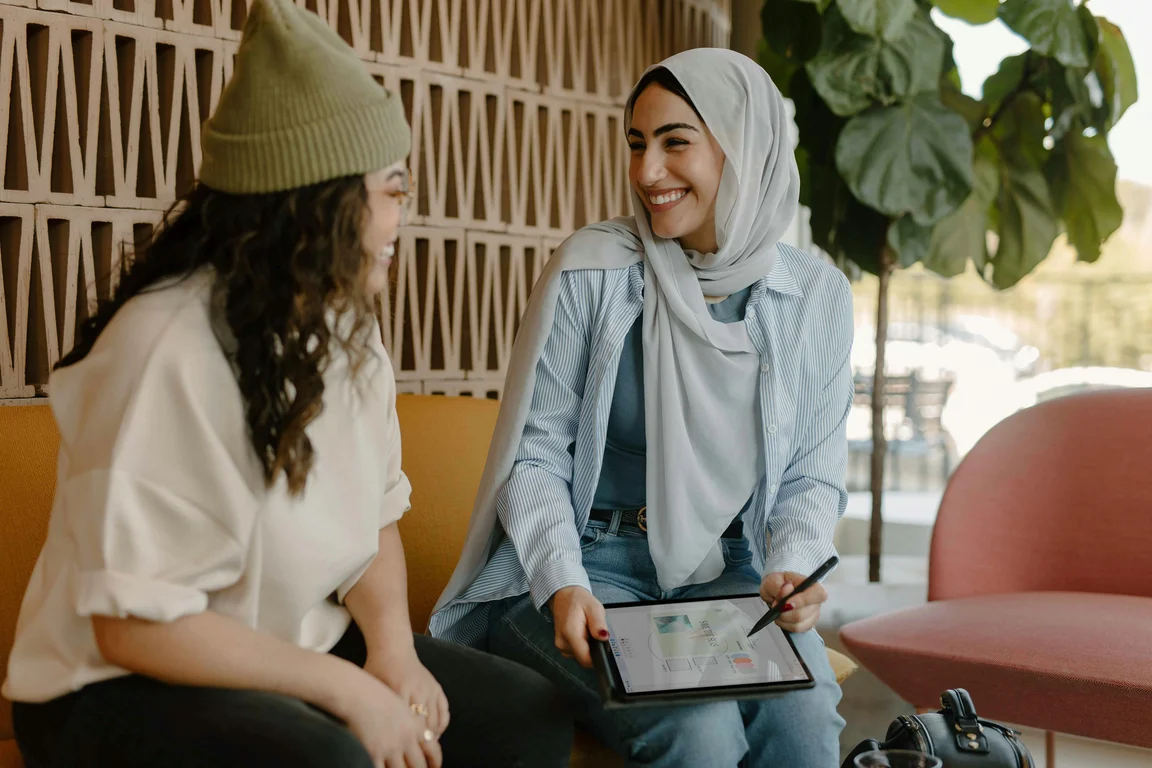 women holding tablet sat next to another women and smiling 