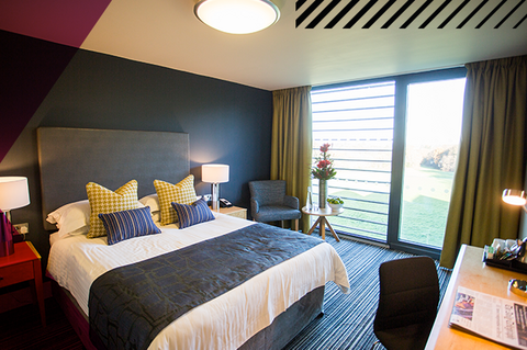 Modern bedroom with contemporary décor, double bed on the left of the room with a large glass window.