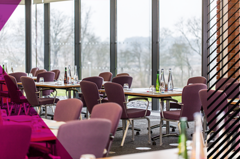 A conference room at Woodland Grange, tables and chairs positioned in front of large floor-to-ceiling windows. Each table has bottles of water.