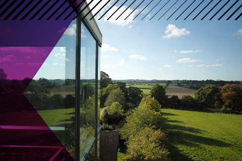 The outside of the Woodland Grange venue with glass windows reflecting the countryside. Hills and fields present in the background.