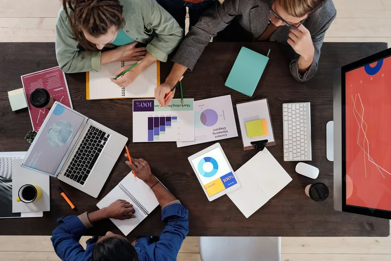 birds-eye view of people working at a desk with laptop and notepads