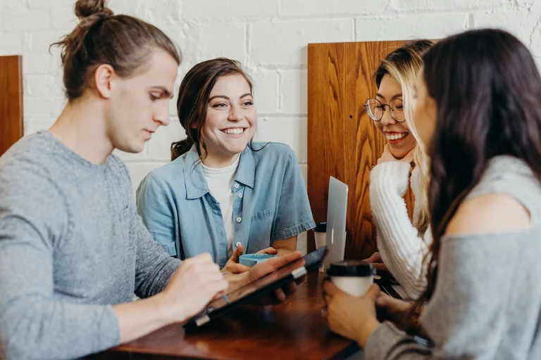 people sat at a table smiling and using laptop and tablet